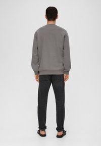 Gray sweatshirt with ribbed cuffs and hem, worn with dark jeans. Plain design, no visible patterns, viewed from the back.