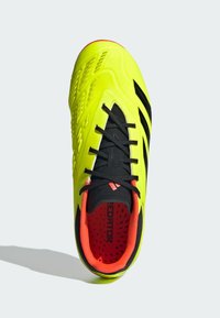 Chaussure de football fluorescente jaune avec des accents noirs, tige texturée, fermeture à lacets et intérieur rouge. Présente un design épuré et des détails moulés.