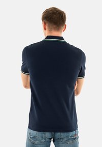 Polo de color marino con cuello y mangas en contraste verde y blanco, hecho de una tela suave, combinado con unos jeans de color azul claro.