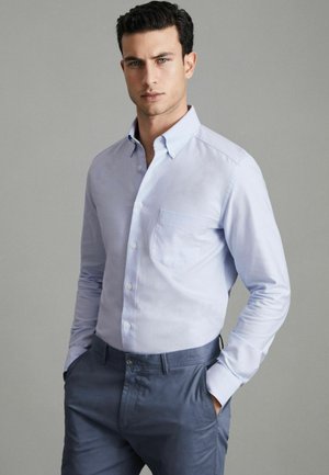 Lichtblauw overhemd met knoopsluiting en kraag, voorzien van een borstzak. Gekozen in combinatie met donkerblauwe broek, die een slim fit ontwerp laat zien.