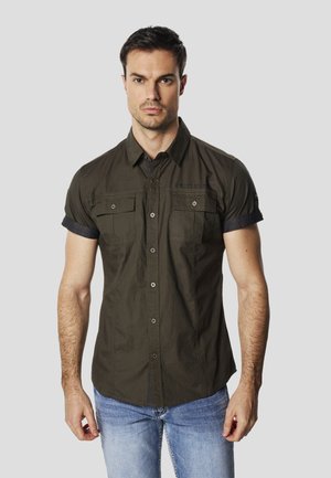 Cămașă cu mâneci scurte, de culoare verde măsliniu închis, cu nasturi pe partea din față, buzunare pe piept și accente bleumarin la manșete. Confecționată dintr-un material ușor.