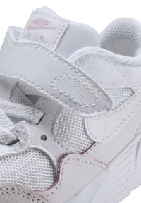 Zapatilla blanca de Nike que presenta materiales de cuero y malla, una correa de velcro, superficies texturizadas y un logo rosa en la lengüeta.
