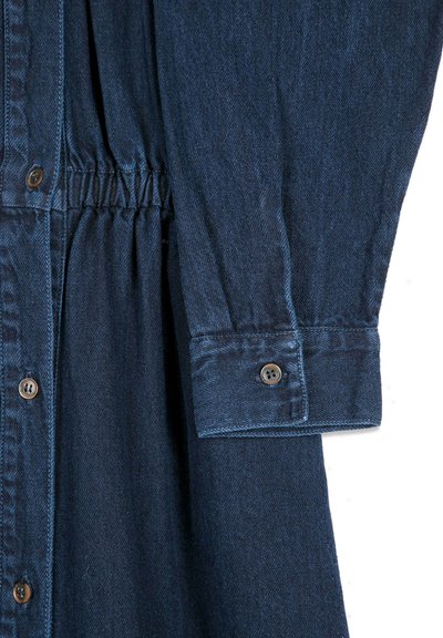 Manche et taille d'une robe en denim bleu foncé avec fronces élastiques et boutons marron au poignet et à l'avant.