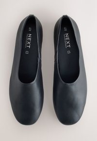 Paire de chaussures plates noires à enfiler, bouts arrondis, étiquetées "NEXT Forever Comfort" et taille 6½ (40), vues de dessus sur un fond neutre.