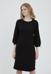 Mustapuku, jossa on tekstuurinen kangas hienovaraisella kuviolla, pyöreä pääntie ja kolmanneksen pituudet hihat.