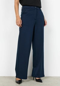 Marineblauwe wijde broek met een gladde textuur, voorzien van een knoopsluiting en twee voorzakken, gecombineerd met zwarte pumps met een puntige neus.