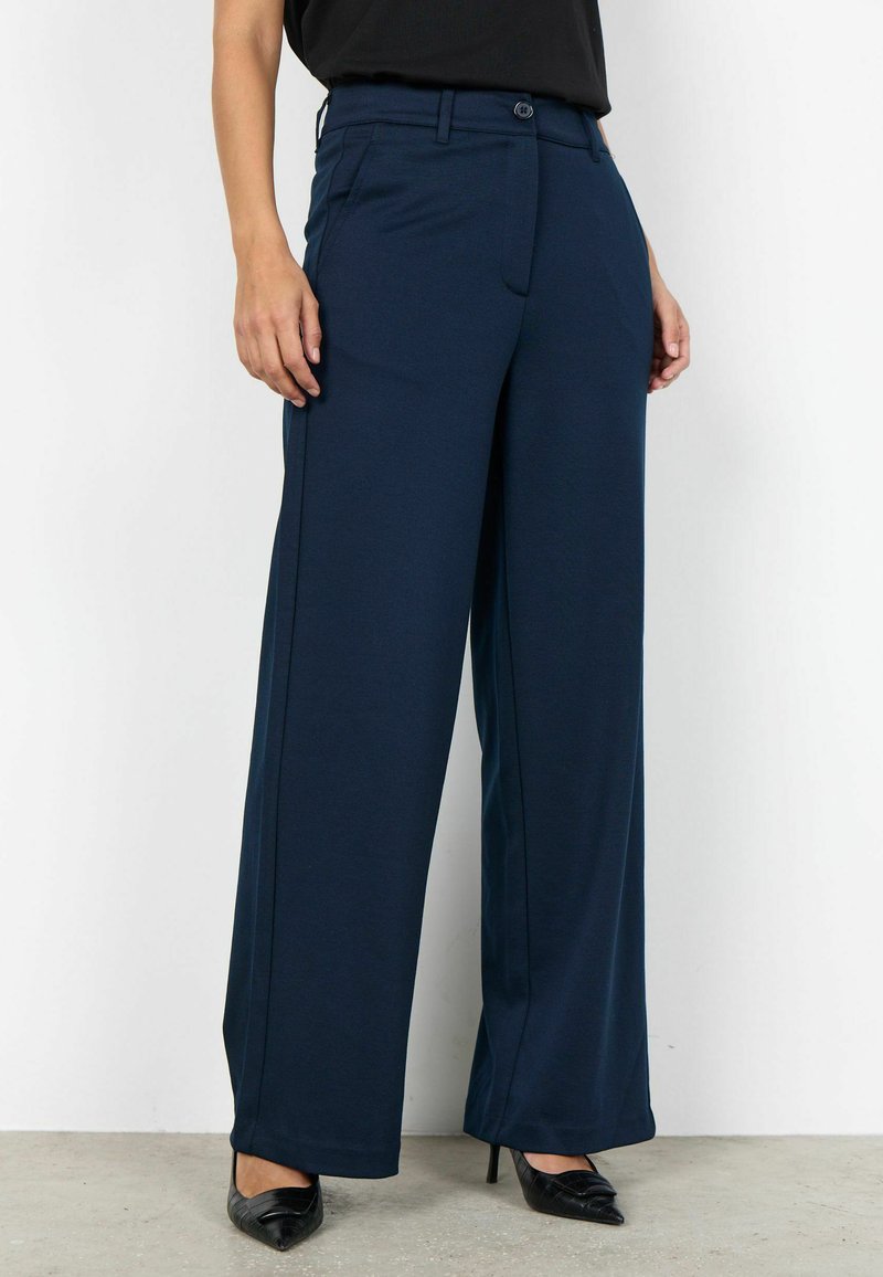 Marineblauwe wijde broek met een gladde textuur, voorzien van een knoopsluiting en twee voorzakken, gecombineerd met zwarte pumps met een puntige neus.