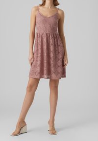 Vestido de encaje en rosa empolvado con tirantes finos, cuerpo ajustado y falda acampanada. Presenta un patrón de diamantes y una tela texturizada.