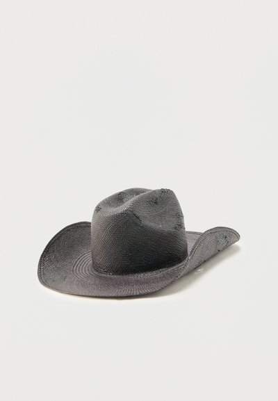 Μαύρο πλεγμένο καουμπόικο καπέλο με φαρδύ, καμπυλωτό γείσο και πιεσμένο στέμμα τοποθετημένο πάνω σε λευκή επιφάνεια.