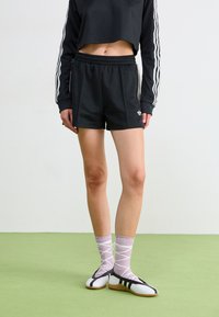 Svarte shorts med elastisk midjebånd, kombinert med en svart cropped langermet topp med hvite striper. Hvite og svarte flate sko, rosa mønstrede sokker.