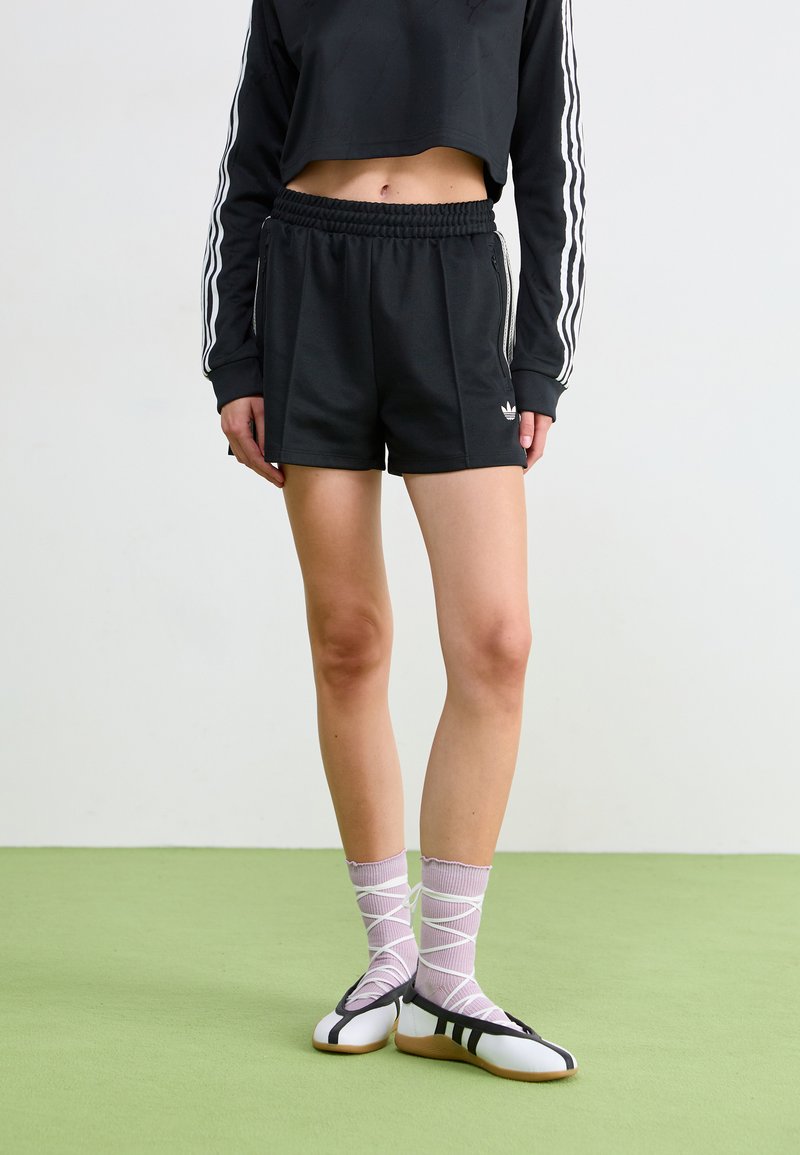 Svarte shorts med elastisk midjebånd, kombinert med en svart cropped langermet topp med hvite striper. Hvite og svarte flate sko, rosa mønstrede sokker.