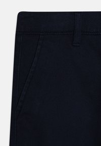 Pantaloni blu navy con una texture liscia, dotati di una cintura e tasche laterali. Il tessuto è resistente con un leggero lucido.