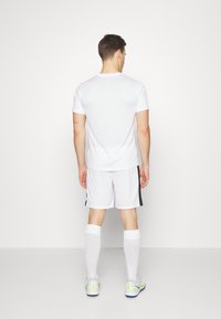 Vitt idrottströja och shorts, tillverkade av lätta material, i kombination med vita strumpor och sneakers med gröna detaljer, sedda bakifrån.