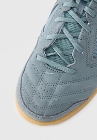 Blue suede sneaker with mesh accents, featuring a round toe, textured surface, and gum rubber sole. Details include decorative stitching and perforations.