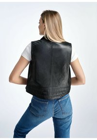 Czarna skórzana kamizelka o gładkiej teksturze, z niskim tyłem i wysokim kołnierzem, w połączeniu z niebieskimi dżinsami.