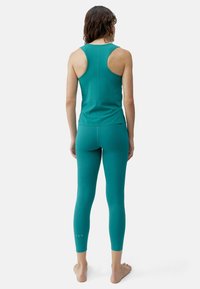 Turkisbla aktive klær sett bestående av en ermeløs topp og tettsittende leggings, med glatt tekstur og presise søm detaljer.