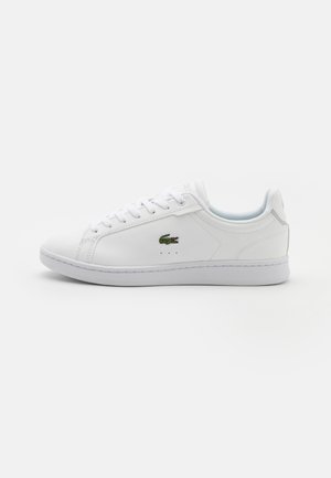 Hvit lær sneakers med flate lisser, rund tå og en lys blå innside. Har en liten grønn krokodillelogo og minimale perforeringer.