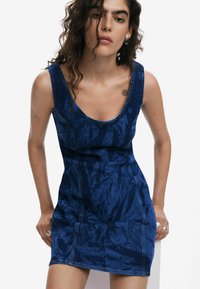 Rochie din denim de culoare albastru închis, cu un design ajustat, decolteu rotund și textură călcată. Prezintă o cusătură vizibilă și un tiv scurt.