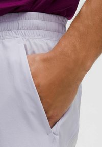 Ljuslila shorts med elastisk midja, med en sidficka. Synlig hand som vilar i fickan och visar tygstrukturen.