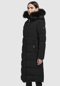 Černý péřový kabát s odnímatelnou umělou kožešinou na kapuci, prošívaná textura, dlouhá délka a dvě boční kapsy. Zapínání na zip a značkové detaily.