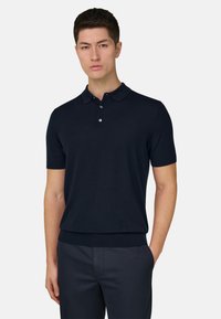 Polo de manga corta color azul marino hecho de tela suave, con cuello clásico, tapeta de tres botones y dobladillo ajustado de canalé.