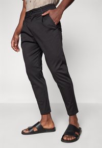 Czarne zwężane spodnie z elastycznym pasem i bocznymi kieszeniami, wykonane z gładkiego materiału. Zestawione z czarnymi sandałami na otwartym palcu.