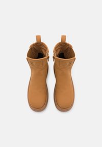 Knöchelhohe Stiefel aus cognacfarbenem Leder mit glatter Oberfläche, abgerundeter Spitze, Zuglaschen und goldfarbenen Metallakzenten. Flache Gummisohlen.