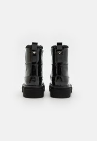 Bottines en cuir verni noir avec bordure en fausse fourrure, fermeture éclair à l'arrière, tirette, semelle épaisse noire et détails cousus.