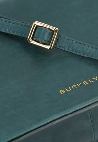 Borsa in pelle verde acqua con una superficie liscia, caratterizzata da una fibbia quadrata dorata e il nome del marchio "BURKELY" impresso in oro.