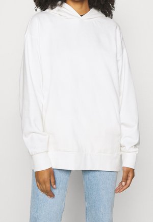 Vit luvtröja i mjuk, texturerad tyg. Har en avslappnad passform, långa ärmar och ribbad fåll. Matchas med ljusblå jeans.