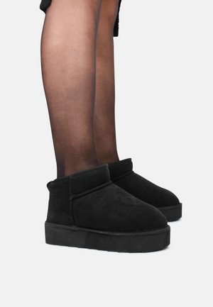 Black suede ankle boots with a flat sole and a stitched band around the top, featuring a minimalist design and smooth texture.