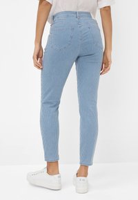 Blauwe gestreepte high-waisted jeans met slim fit, textuurstof, twee achterzakken en gestyled met witte sneakers voor een casual look.