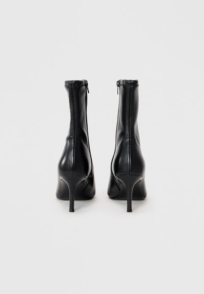 Czarne skórzane botki za kostkę z zapięciem na zamek, z wysokim obcasem typu stiletto i gładką powierzchnią, przedstawione z widoku z tyłu.