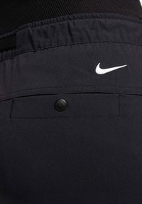 Černé sportovní šortky z hladké tkaniny, s elastickým pasem a malým bílým logem Nike. Obsahují také detail kapsy na knoflík na zadní straně.