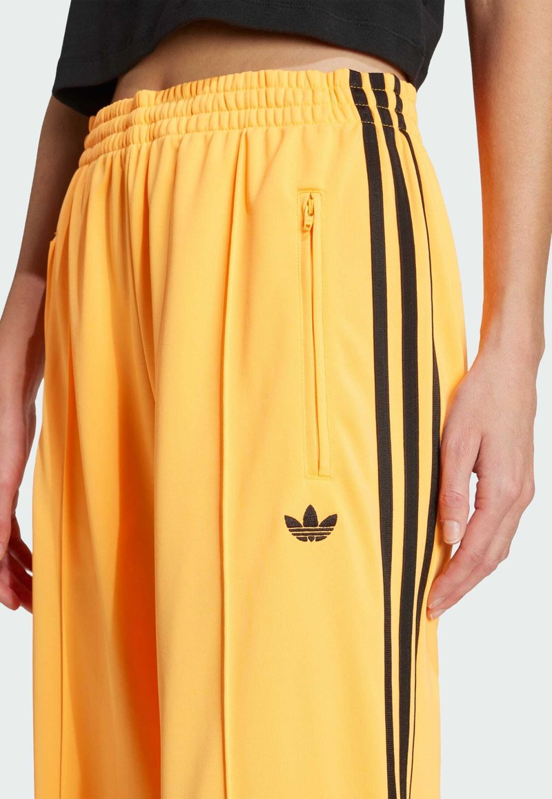 Gelbe Sporthose mit einem gerafften Bund, schwarzen seitlichen Streifen, einer Reißverschlusstasche und einem kleinen schwarzen Logo an der linken Hüfte.