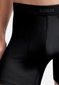 Svarta Sloggi boxer shorts har ett slätt, elastiskt tyg med en bred midja som visar varumärket, designade för komfort och stöd.