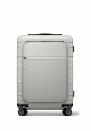 Compact silver hard-shell suitcase with front zip pocket, four black spinner wheels, and top handle, standing upright on white background.