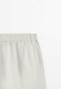 Jupe beige clair avec taille élastique montrant un tissu froncé et un détail de passants de ceinture sur un fond uni.