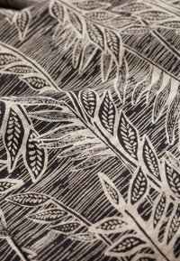 Bomullstyg med ett mönster av svarta och krämfärgade löv, med intrikata linjedetaljer och en texturerad yta. Organisk, naturinspirerad design.