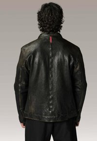 Veste en cuir noir avec une finition texturée, des poignets zippés et une couture marquée dans le dos, agrémentée d'une étiquette rouge au col.
