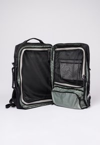 Black backpack with an open interior. Features mesh pockets and a green inner lining. Zippers and pull tabs visible. Adjustable straps.