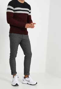 Pull en tricot avec un corps bordeaux et des rayures noires et blanches ; associé à un pantalon gris ajusté et des chaussures de sport blanches.