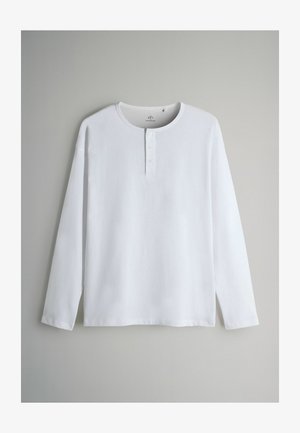 White long-sleeve henley shirt made of soft cotton, featuring a crew neckline, three-button placket, and side slits at the hem.