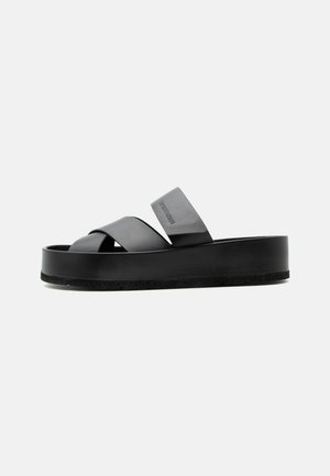 Black platform slide sandal with two wide leather straps crossing over the foot and a large strap near the ankle.