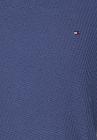 Polo shirt di colore blu navy con texture, caratterizzato da un piccolo logo rosso, bianco e blu sul lato sinistro del petto. Il tessuto presenta un sottile motivo a rombi.