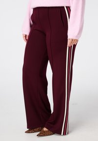 Bordeaux wijde broek met zijstrepen in crème en donkerroze. Gemaakt van zacht materiaal, met voorzakken en een getailleerde pasvorm.