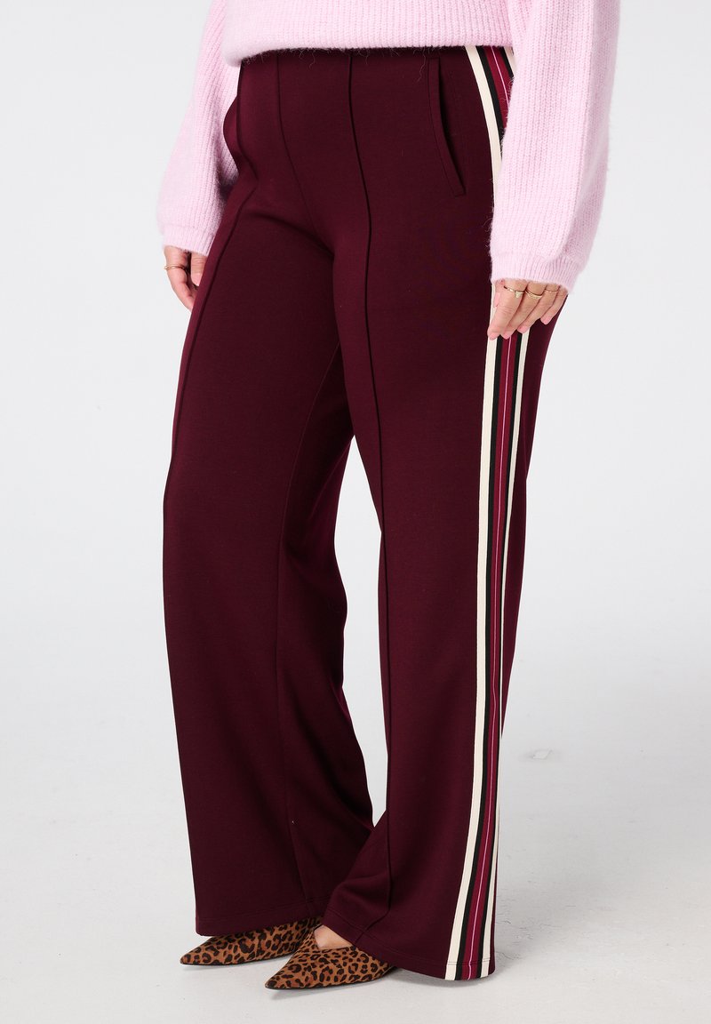 Bordeaux wijde broek met zijstrepen in crème en donkerroze. Gemaakt van zacht materiaal, met voorzakken en een getailleerde pasvorm.