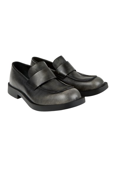 Paire de mocassins noirs en cuir à enfiler, avec des bouts arrondis et des semelles épaisses en caoutchouc, sur un fond blanc.