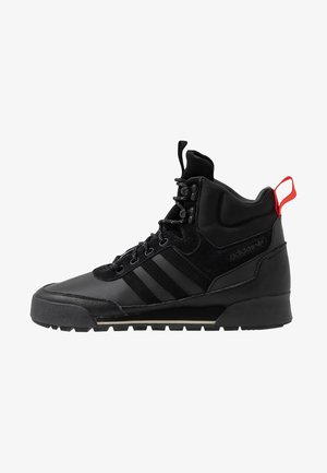 Baskets montantes noires avec bandes Adidas, lacets à l'avant, semelle robuste, col rembourré à la cheville et languette rouge au talon.
