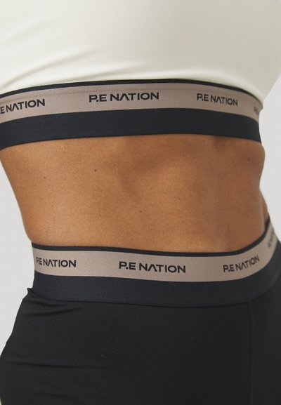 Pantaloni attivi neri con una cintura larga decorata con il logo "P.E NATION" in beige e nero. Tessuto liscio con un design aderente.